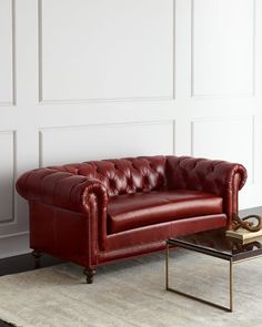 a red leather couch sitting on top of a white rug next to a coffee table