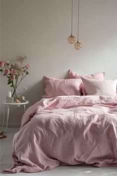 a bed with pink sheets and pillows in a white room next to a flower vase