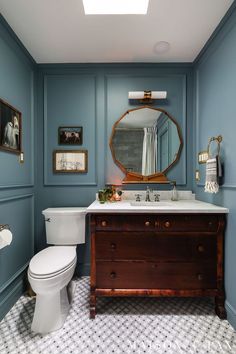 a bathroom with blue walls, white toilet and wooden vanity in the center is an oval mirror