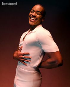 a man with his hands on his hips smiling at the camera while standing in front of a dark background