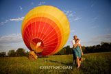 a man and woman standing next to each other in a field with a large hot air balloon