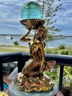 a statue on top of a table with a glass ball in the shape of a mermaid