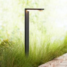 an outdoor light that is on the side of a brick wall near some tall grass