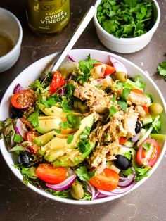 a salad with chicken, olives, tomatoes and lettuce in a white bowl