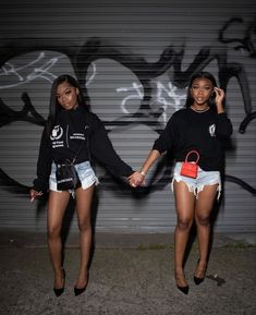 two young women holding hands and walking in front of graffiti