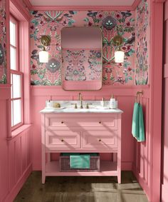 a pink bathroom with floral wallpaper and gold accents on the mirror above the sink