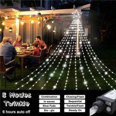 an outdoor christmas tree with white lights on it and people sitting at a table in the background