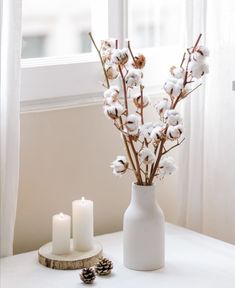 a white vase filled with cotton sitting on top of a table next to two candles