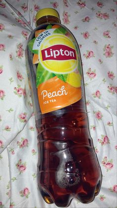 a bottle of lipton peach tea sitting on top of a floral covered bed sheet