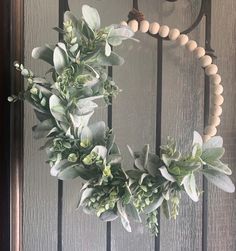 a wreath is hanging on the front door with wooden beads and greenery around it