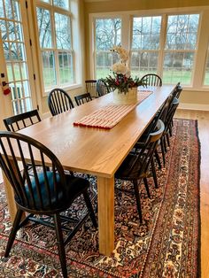 a dining room table with chairs and a rug in front of the large windows that look out onto an open field