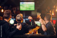 three men are sitting at a bar and one is holding up a drink in the air