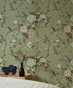 two vases with flowers on a table in front of a wallpapered room