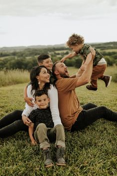 a man, woman and two children are sitting in the grass with their arms around each other