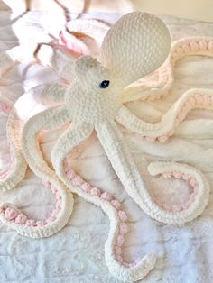 an octopus made out of crochet on a bed with pink and white sheets