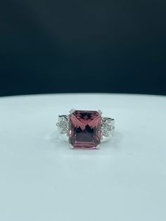 a pink tourmaline and diamond ring sitting on a white surface with black background