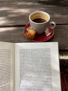 an open book and cup of coffee sit on a wooden table with a red saucer