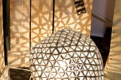 a white vase sitting on top of a wooden table next to a wall with the sun shining through it