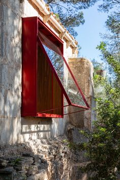 an open window on the side of a stone building with red shutters and metal bars