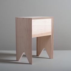 a small wooden table sitting on top of a white floor next to a gray wall