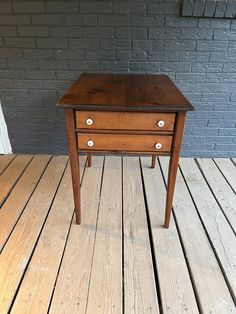 a small wooden table sitting on top of a wooden floor next to a brick wall