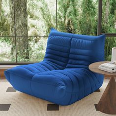 a blue chair sitting in front of a window next to a table with a laptop on it