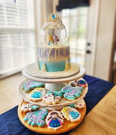 a three tiered cake with frosting and decorated cookies on the bottom, sitting on a table