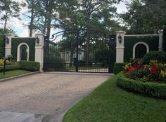 a gated entrance to a home with flowers in the foreground and trees on either side