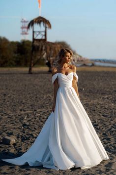 a woman standing on top of a sandy beach wearing a white dress and holding her hand in her pocket