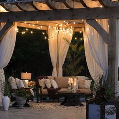 an outdoor living area is lit up with string lights and decorated in shades of white