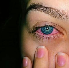 a close up of a person's eye with their hand on her face and the eyes are blue