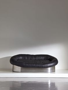 a black leather chair sitting on top of a white floor in front of a wall