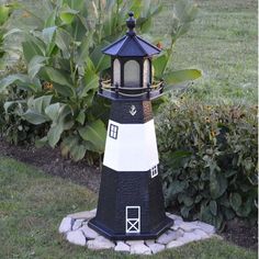 a black and white light house sitting in the middle of a garden next to bushes