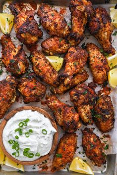 chicken wings with lemon wedges and tzatzh on a baking sheet topped with sour cream