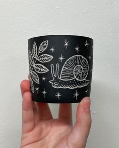 a hand holding up a black and white cup with a snail on it's side