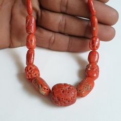 a hand holding a necklace made out of coral beads