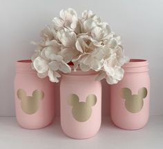 three pink mason jars with gold mickey ears painted on them and flowers in the middle