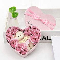 a heart shaped box filled with pink roses and a teddy bear