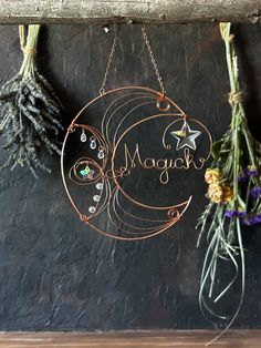 three metal ornaments hanging on a wall next to some dried flowers and herbs with the word magic written in cursive writing