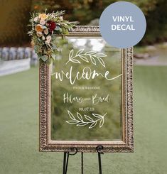 a welcome sign with flowers and greenery is displayed in front of a green field