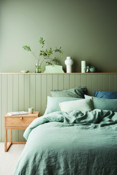 a bed with green sheets and pillows next to a wooden shelf filled with potted plants