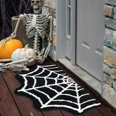 a skeleton sitting on a porch next to a pumpkin and spider web rug with a jack - o - lantern in the background