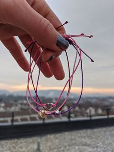 a person holding onto some kind of bracelet with hearts on it's end and the sky in the background