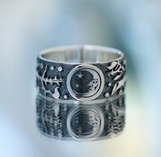 two silver rings with designs on them sitting on top of a glass surface, in front of a blurry background