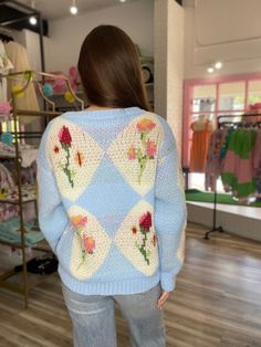 a woman standing in front of a clothing rack with flowers on it's sweater