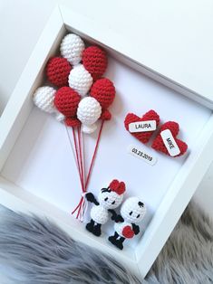 two red and white crocheted hearts in a box with balloons attached to them