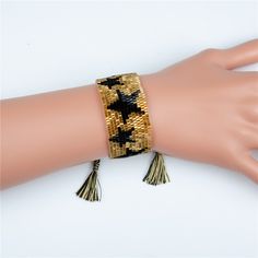 a woman's hand wearing a gold bracelet with black stars and tassels