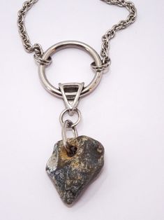 The necklace is made of a decorative silver chain. In the middle there is a metal circle with a diameter of 3 cm, a metal element connected to a natural stone of irregular shape. There is one hole in the stone, gray with a touch of beige. The stone comes from a beach in southern England. In Celtic culture, stones with holes, the so-called The Hag Stone or Odin Stone were good luck amulets that protected against negative energy.  The stone measures 3.3 x 2.6 cm.  A unique gift, unisex. Silver Jewelry With Large Round Stone, Spiritual Necklaces With Round Natural Stones, Silver Chain Pendant Amulet Necklace, Sterling Silver Pendant With Raw Stone, Agate Round Pendant Amulet Jewelry, Silver Agate Amulet Necklace, Unique Sterling Silver Necklace With Raw Stone, Silver Pendant With Raw Stone, Raw Stone Silver Pendant Jewelry