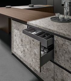 an open drawer in the middle of a kitchen counter with marble worktops and cabinets