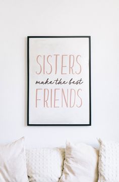 a white couch with pillows and a framed poster on the wall above it that says sisters make the best friends